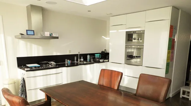 Witte keuken met hoge kast en ovens in de aanbouw, rand van de lichtkoepel zichtbaar