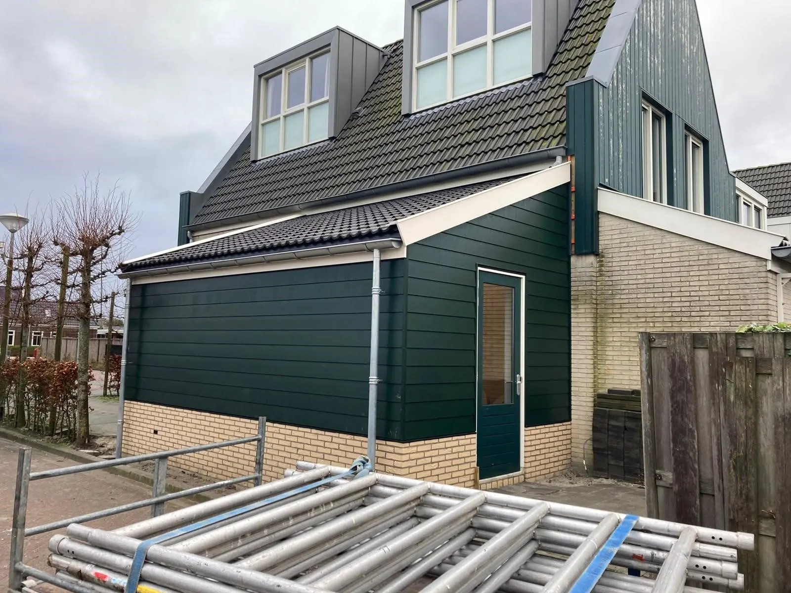 Aanbouw met donkergroene houten gevel, plint van gele baksteen en groene deur in Sijbekarspel