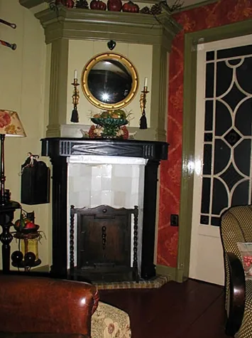 Schouw met zwarte mantel, witte tegels en ronde spiegel naast een deur met glas in bogen