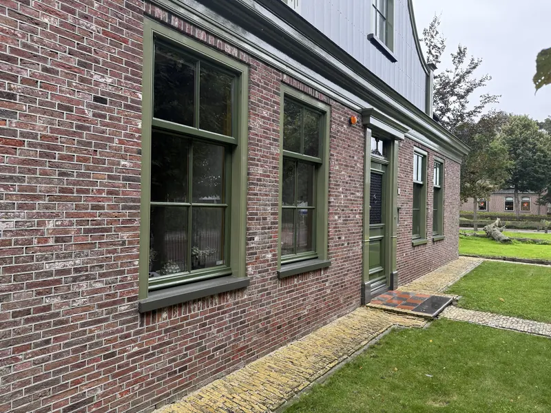 Voorgevel van rode baksteen met olijfgroene kozijnen en voordeur, stolpboerderij in Opmeer