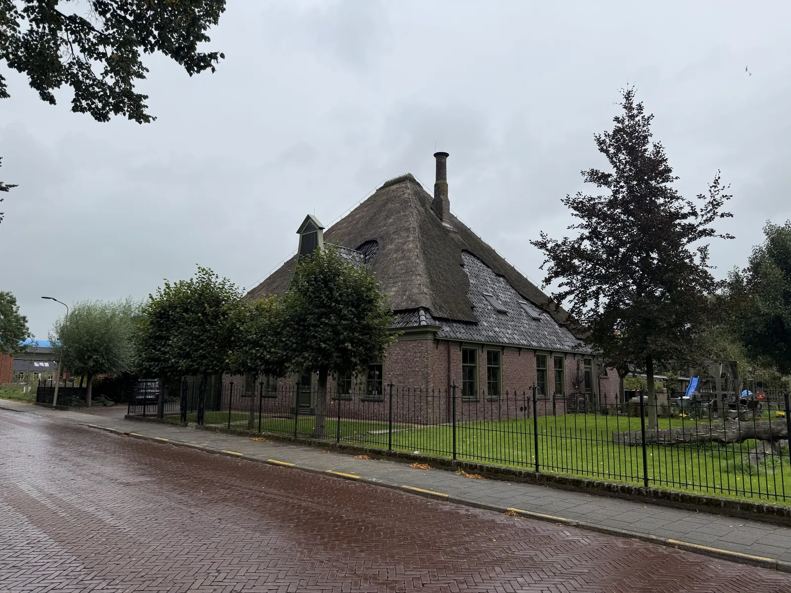 Stolpboerderij in Opmeer met rieten kap, schoorsteen en smeedijzeren hek langs de straat