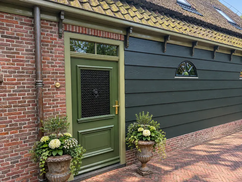 Groene deur met smeedijzeren rooster tussen baksteen en donkergroen potdekselwerk, stolpboerderij in Opmeer