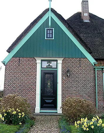 Groene beschoten topgevel boven de voordeur met witte pilasters, stolpboerderij in Sijbekarspel