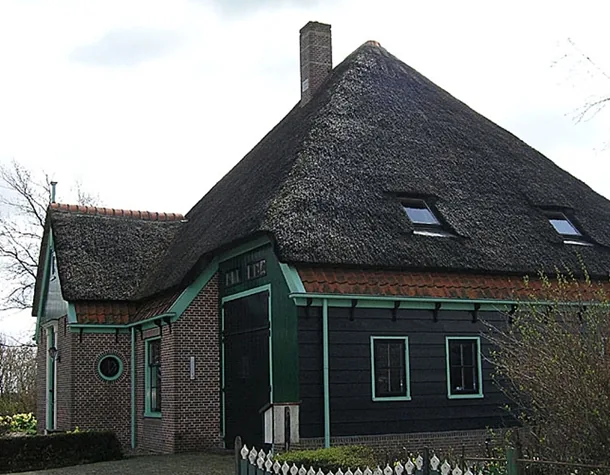 Zijkant van de stolpboerderij in Sijbekarspel met rond venster, donkere schuurdeur en dakramen in het riet