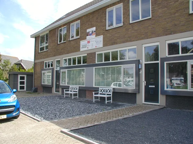 Voordeuren en ramen in grijze kaders met witte bankjes ervoor, voormalige brandweerkazerne in Spanbroek
