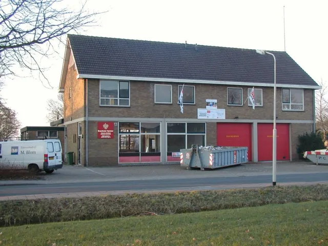 De brandweerkazerne in Spanbroek voor de verbouwing, met twee rode roldeuren en een container ervoor