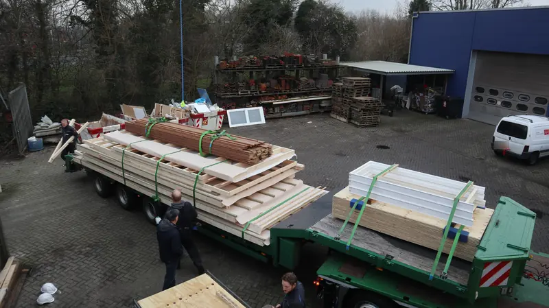 Prefab wanden, kozijnen en houten delen op een dieplader, klaar voor vervoer naar de dakopbouw