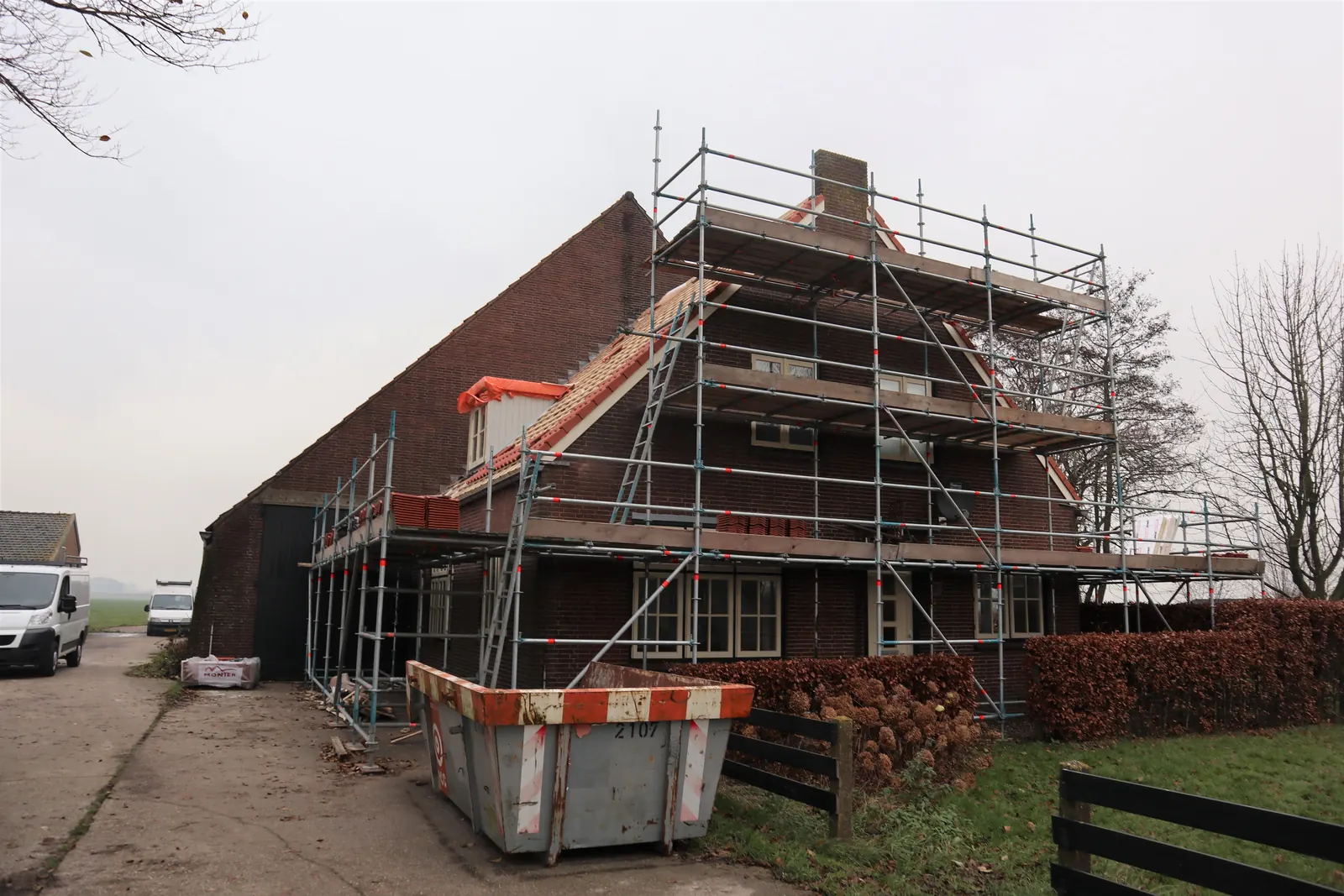 Bakstenen woning in Obdam rondom in de steigers tijdens de dakrenovatie, container op de oprit