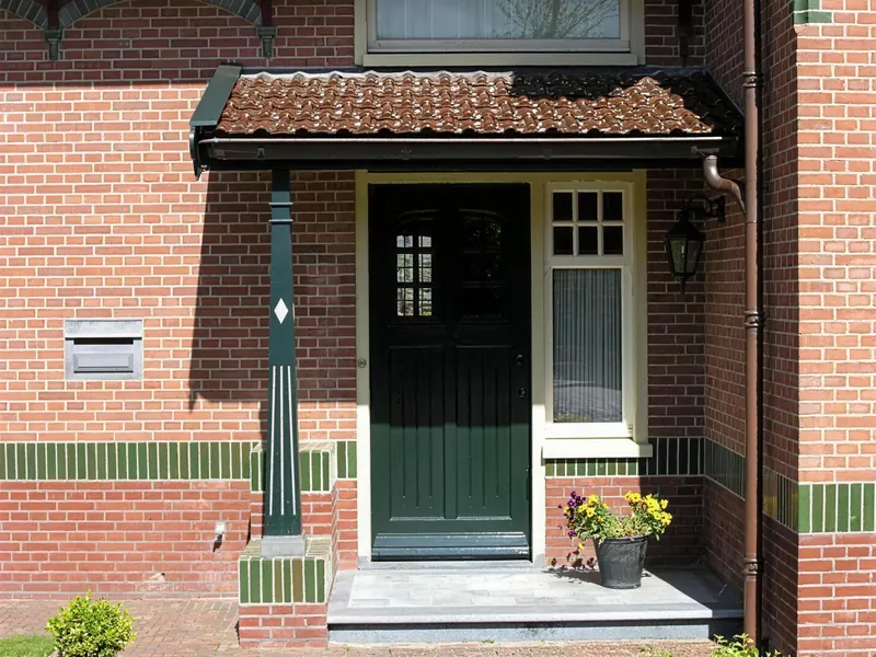 Groene voordeur onder een luifel met pannen en een groene paal
