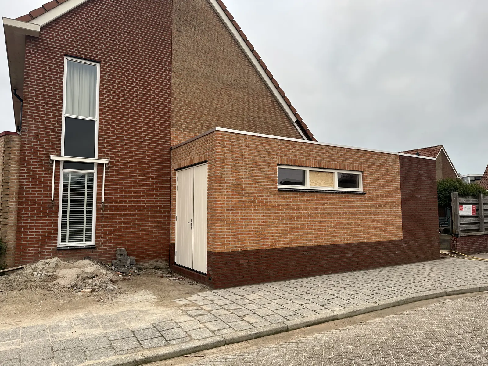 Gemetselde garage naast een woning in Spanbroek met witte dubbele deuren en een raamstrook