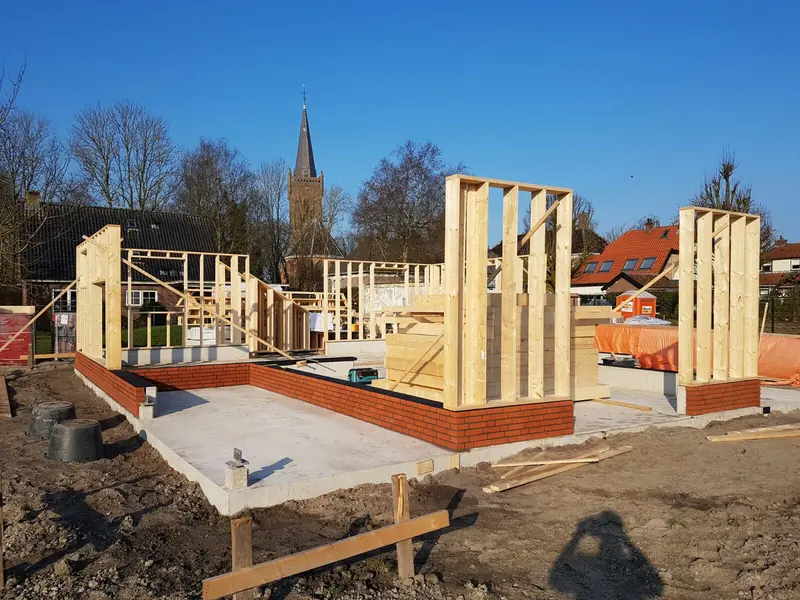 Houtskeletwanden op de gemetselde plint, met de kerktoren van Hoogwoud op de achtergrond
