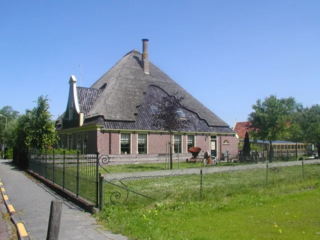 Stolpboerderij in Opmeer met rieten kap en smeedijzeren hek langs het trottoir, oudere foto