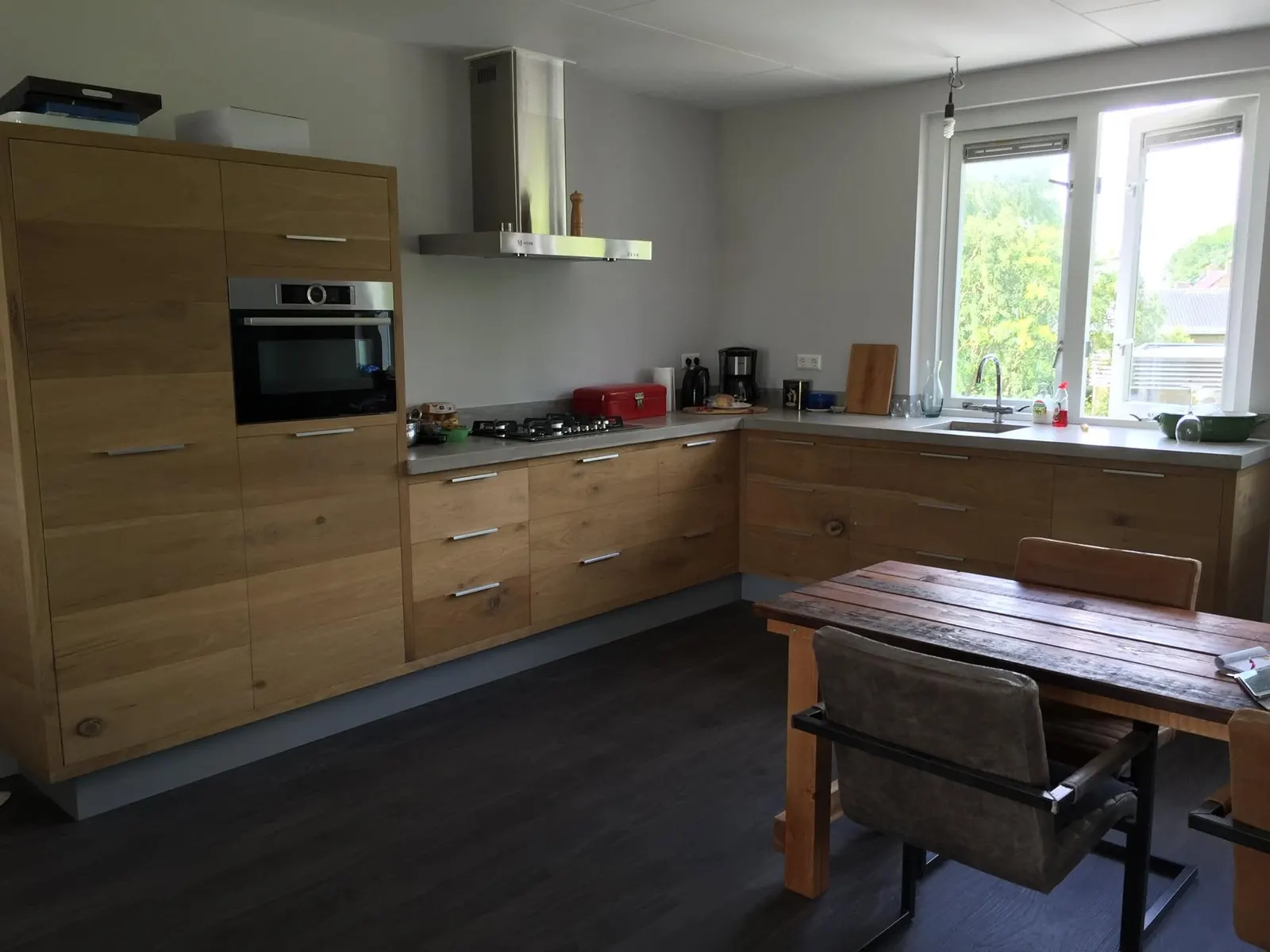 Hoekkeuken in Spanbroek met eiken fronten, betonnen werkblad, hoge kast met oven en RVS afzuigkap