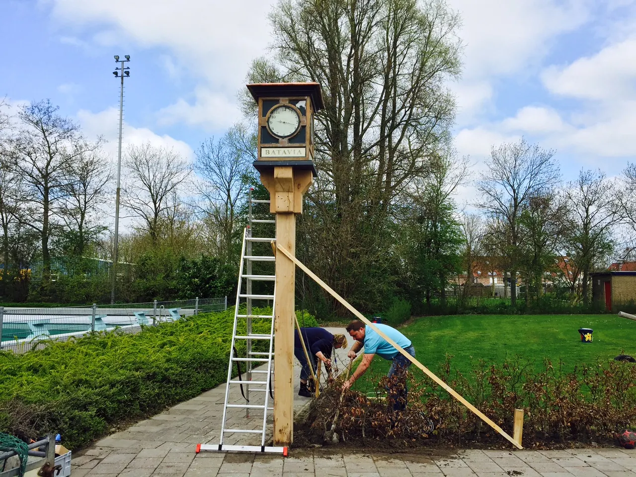 Klok met opschrift Batavia op een houten paal bij zwembad 't Woudmeer, met ladder en schoren
