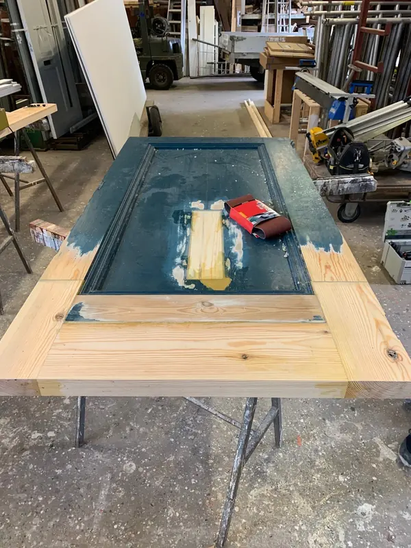 Geschuurde paneeldeur van het raadhuis in Hoogwoud met nieuw hout aan de onderkant, in de werkplaats