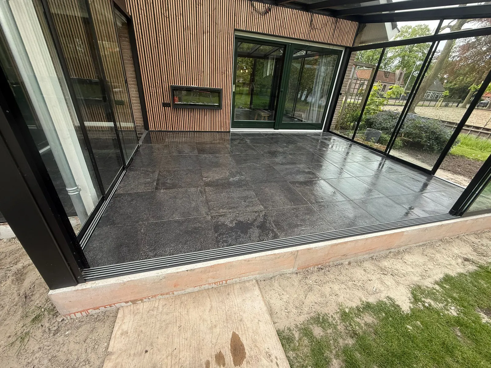 Serre in Obdam met glazen schuifwanden, donkergrijze tegelvloer en wand van verticale houten latten