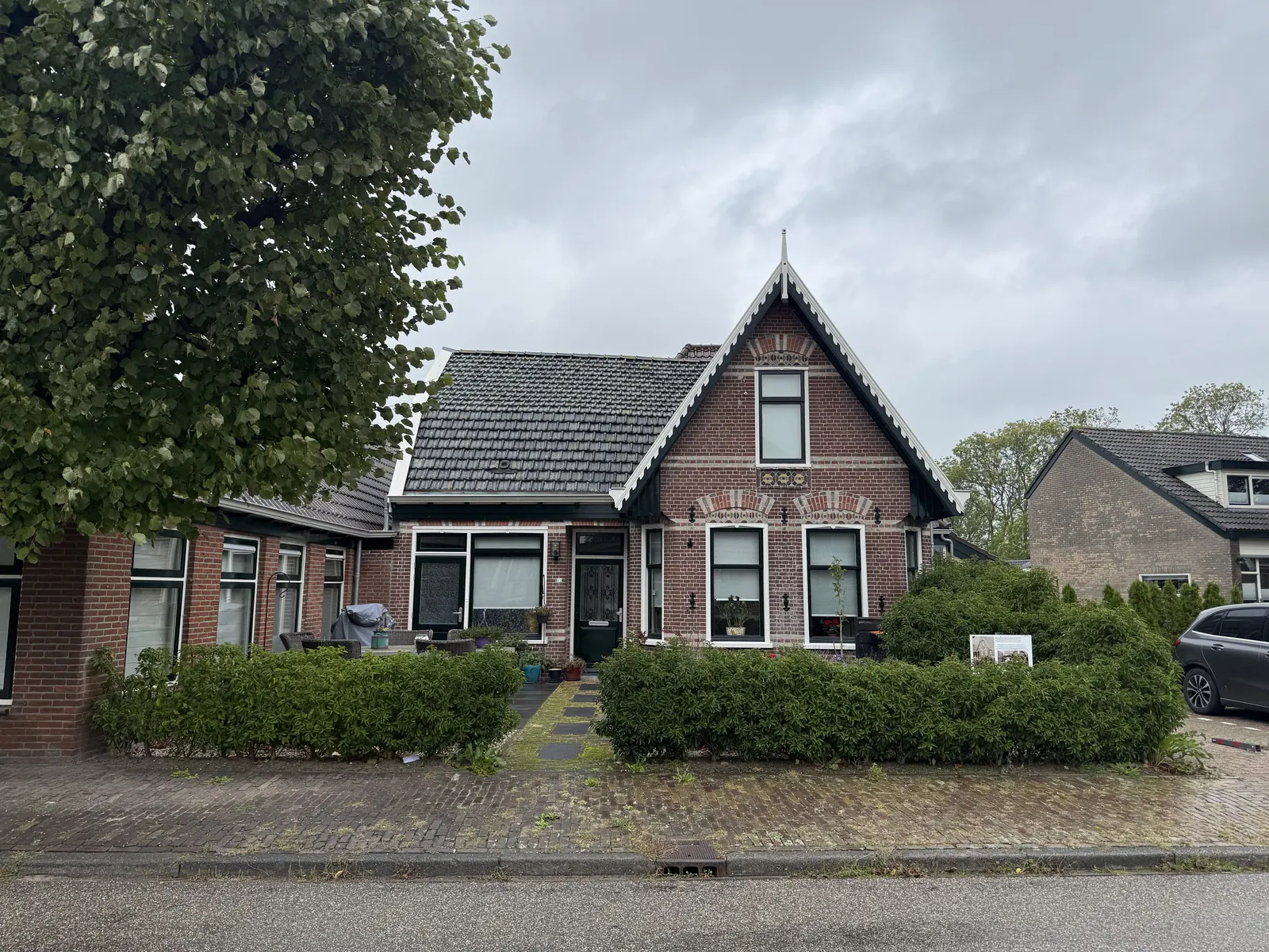 Voorhuis van baksteen met siermetselwerk, witte windveren en makelaar, voormalig café