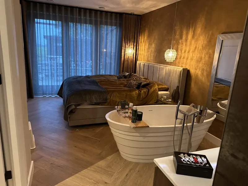 Slaapkamer met vrijstaand bad, visgraatvloer en hoge gordijnen voor de schuifpui, Oosthuizen
