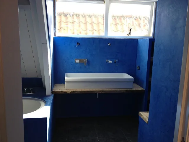 Blauwe badkamer in Alkmaar met brede witte wasbak op een oude houten plank onder het raam