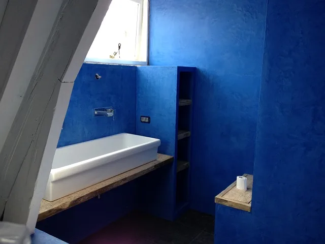 Brede wasbak op houten plank en open vakken in de blauwe badkamerwand, Alkmaar