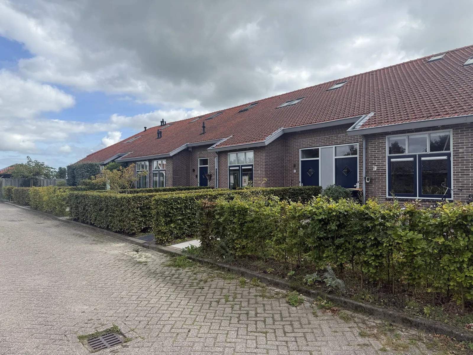 Zeven woningen in het voormalige verenigingsgebouw in Hoogwoud, met rood pannendak en voortuinen met hagen