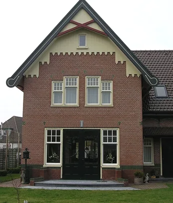 Achtergevel van de villa in Spanbroek met donkere dubbele deuren en crèmekleurige geveltop met rood kruis