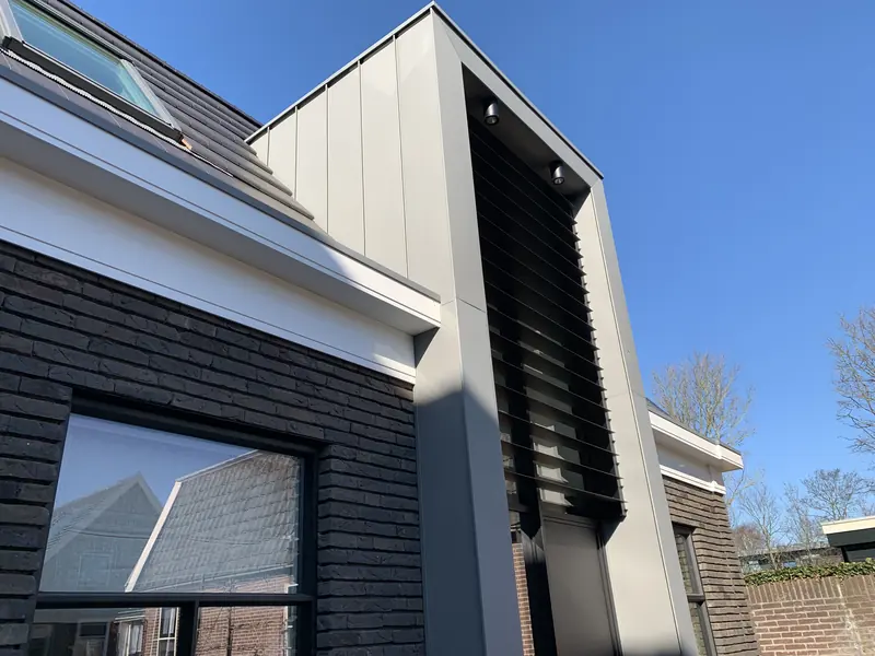 Entreepartij met zwarte lamellen en spots tussen witte daklijst en donkere baksteen, Broek op Langedijk