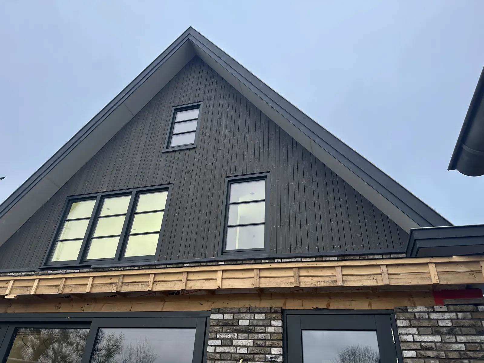 Topgevel met donkere verticale houten delen en antraciet kozijnen boven grijze baksteen, woonhuis in Obdam