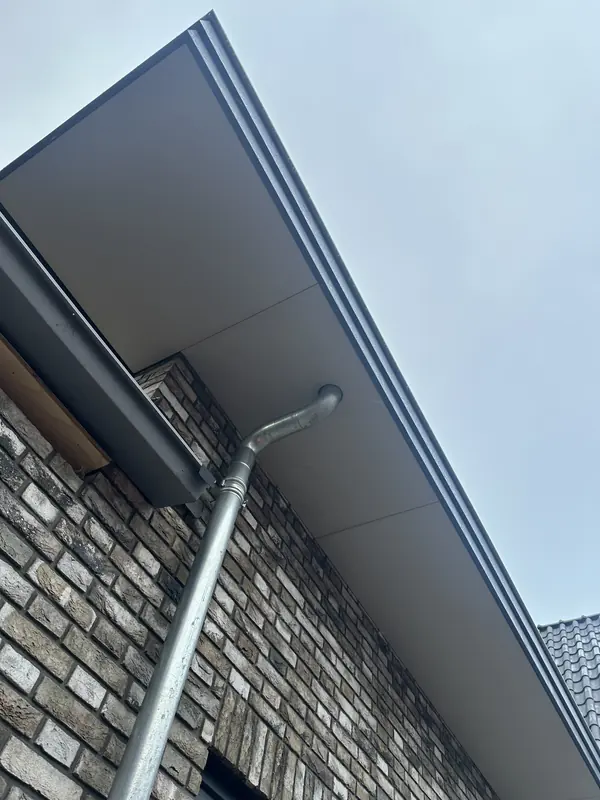 Overstek met antraciet goot en zinken regenpijp tegen grijze baksteen, woonhuis in Obdam