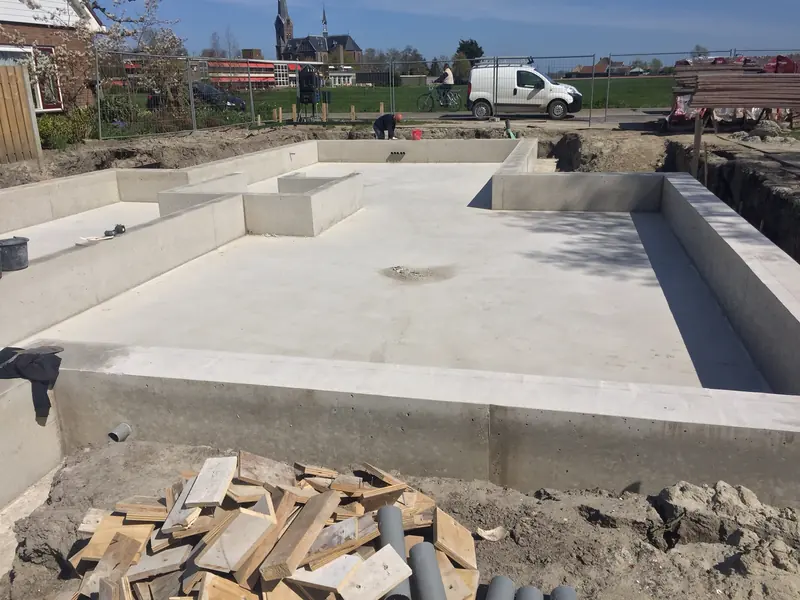 Betonnen fundering en begane grondvloer van het woonhuis in Spanbroek, met de kerk op de achtergrond