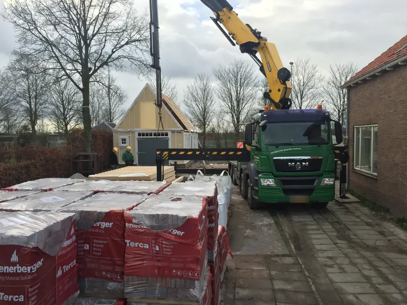 Kraanwagen lost stenen op de bouwplaats in Spanbroek, met de schuur in aanbouw erachter