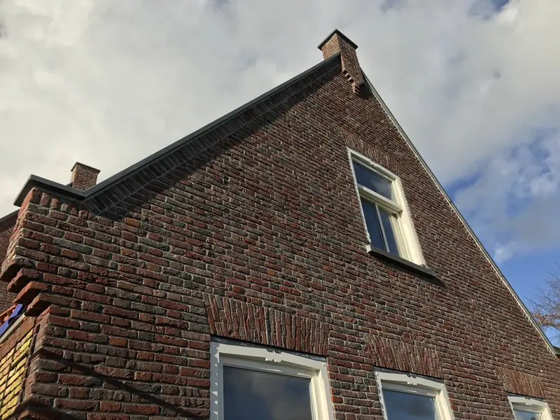 Topgevel van roodbruine baksteen met vlechtwerk, schoorsteen en witte kozijnen, woonhuis in Spanbroek