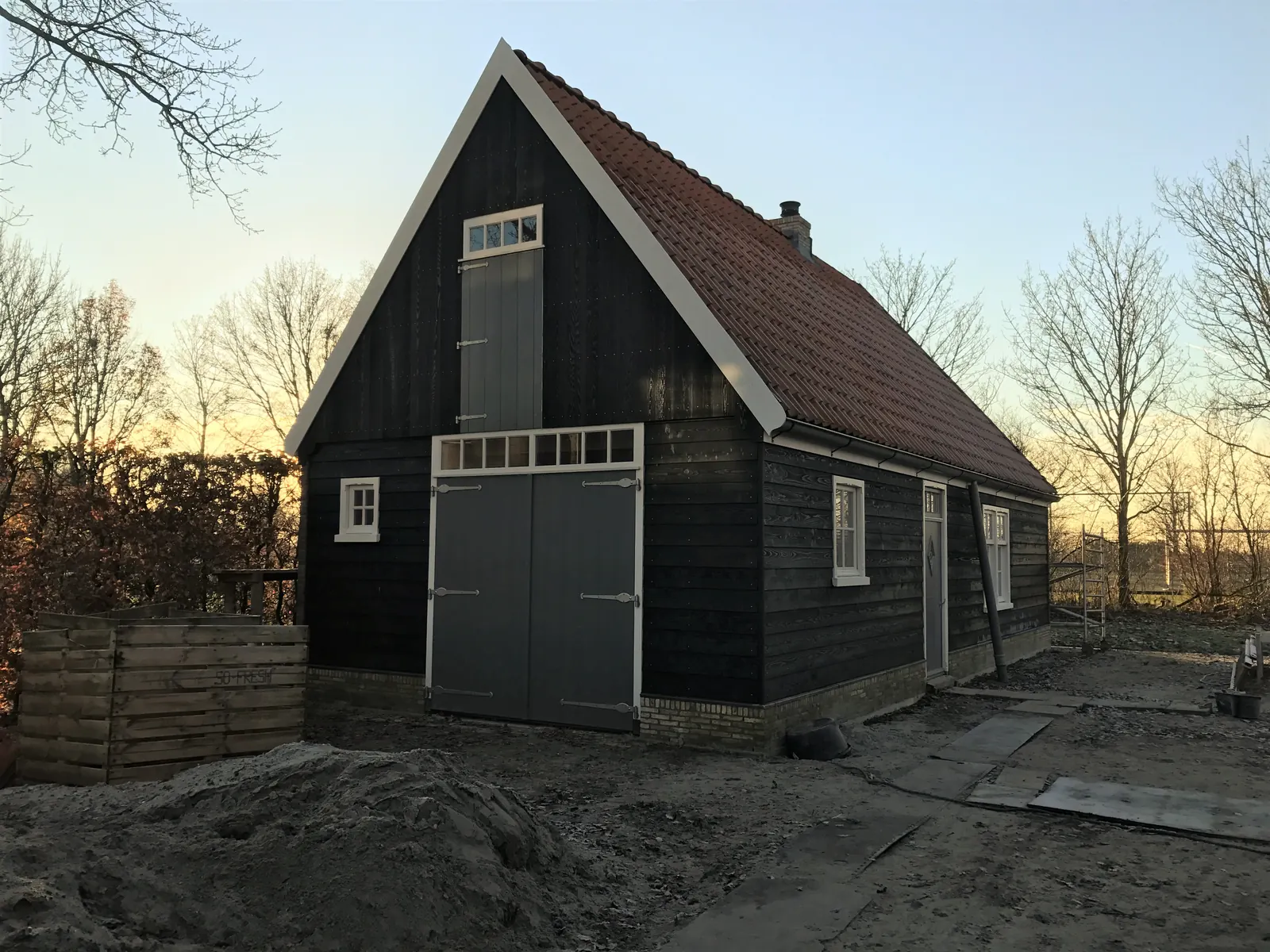 Schuur van zwarte houten delen met grijze openslaande deuren, luik en oranje pannen, Spanbroek