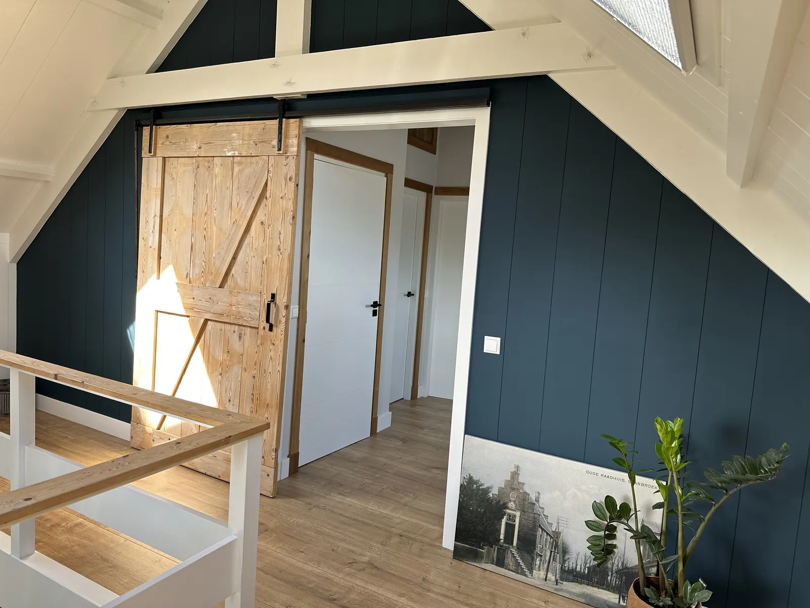 Zolder in Spanbroek met houten schuifdeur aan zwarte rail, blauwe wandbetimmering en witte balken
