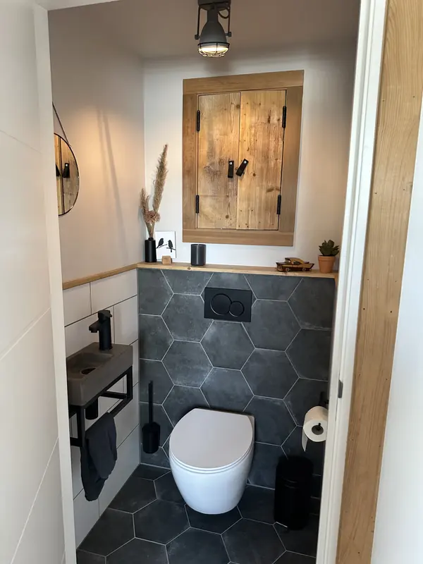 Toilet in Spanbroek met zeshoekige donkere tegels, hangend toilet en houten kastje boven de fontein